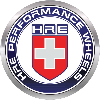 HRE Performance Wheels logo featuring a metallic circular badge with a red shield and white cross in the center, surrounded by a blue ring with the text “HRE Performance Wheels.”