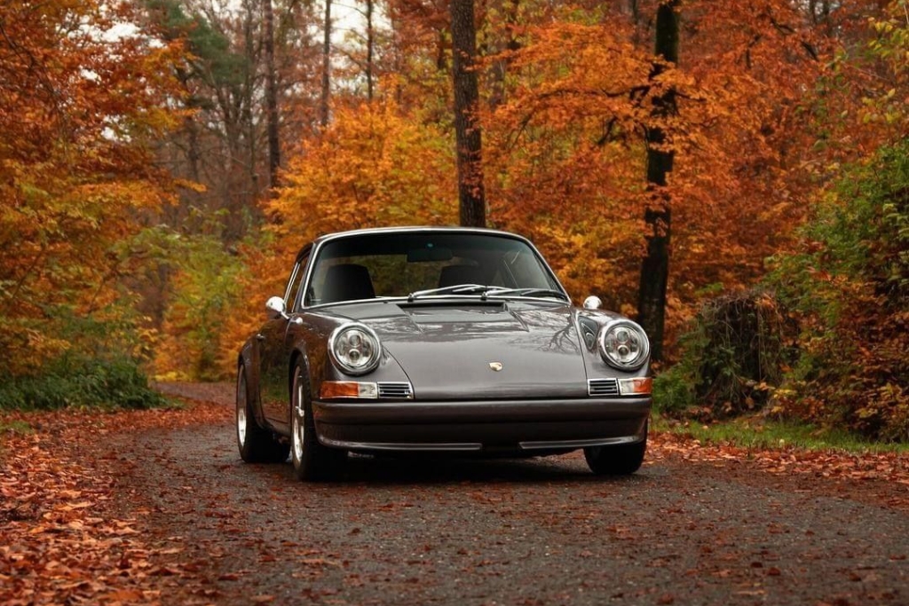 Classic gray Porsche parked on a leaf-covered forest road surrounded by vibrant fall foliage. The autumn setting highlights ideal weather conditions in Dallas for vinyl wrapping installation.