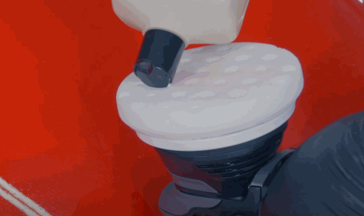 A close-up of a person applying wax onto a foam pad attached to a dual-action polisher, prepping it for car paint correction.