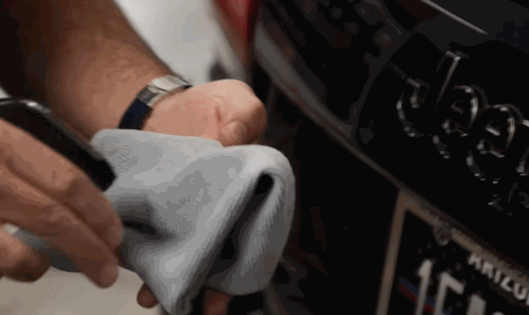 A person uses a microfiber towel to clean the Jeep emblem on the front grille, likely prepping for ceramic coating or wax application.