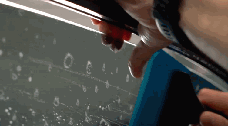 Close-up of a hand smoothing out air bubbles with a squeegee while applying window tint film to a car window.