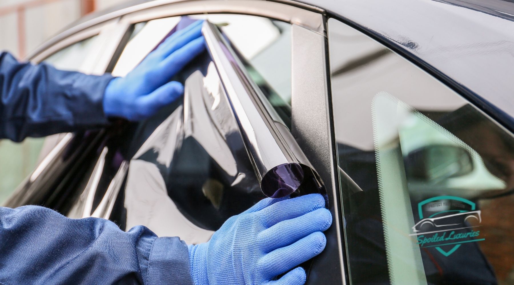 Technician applying window tint film to a car door window at Spoiled Luxuries in Dallas, TX