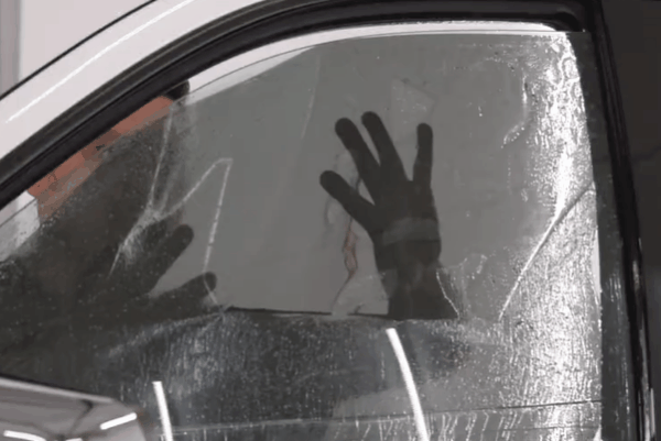 Close-up of a car side window during wet window tint installation with film being smoothed into place